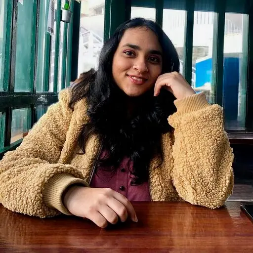 Portrait of Trishadhi Reddy Palwai, Mentor(SHE:) Operations Coordinator, pictured sitting at a desk with large windows in the background.