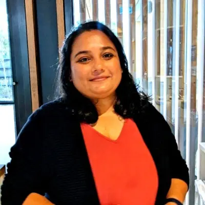 Portrait of Trishadhi Reddy Palwai, Mentor(SHE:) Operations Coordinator, pictured sitting at a desk with large windows in the background.
